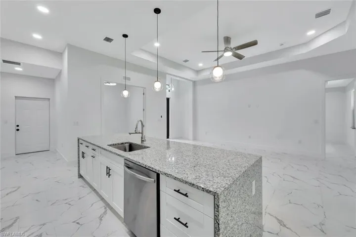Kitchen featuring dishwasher, ceiling fan, a raised ceiling, white cabinetry, and light marble finish floors