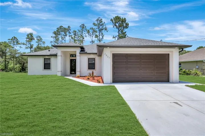 Prairie-style home with driveway, a front yard, a garage, a shingled roof, and stucco siding