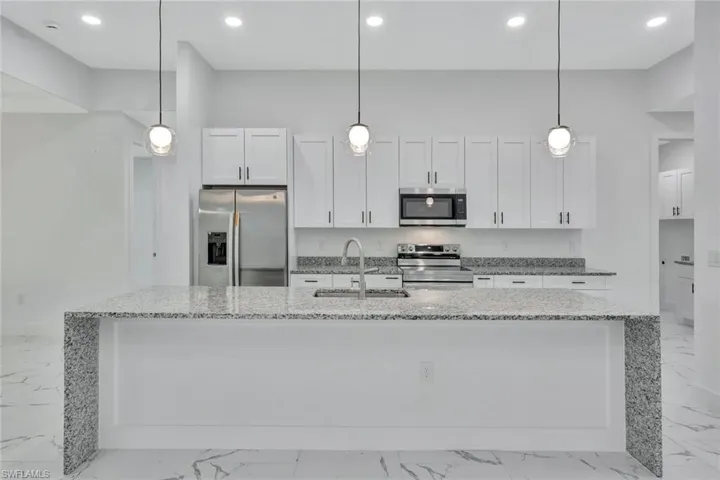 Kitchen featuring appliances with stainless steel finishes, light marble finish floors, light stone countertops, and recessed lighting