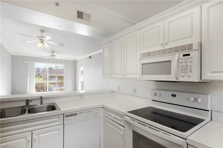 Kitchen featuring white appliances, white cabinetry, ornamental molding, light countertops, and ceiling fan