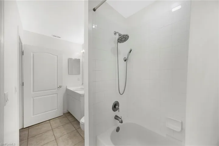 Bathroom with washtub / shower combination, light tile patterned floors, and vanity