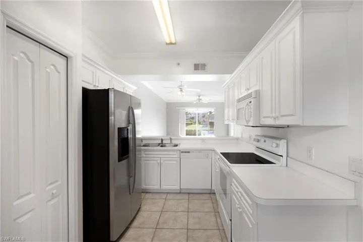 Kitchen with white appliances, white cabinets, light tile patterned flooring, light countertops, and crown molding