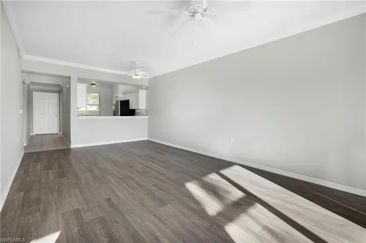 Unfurnished living room with crown molding, dark wood-style floors, and ceiling fan