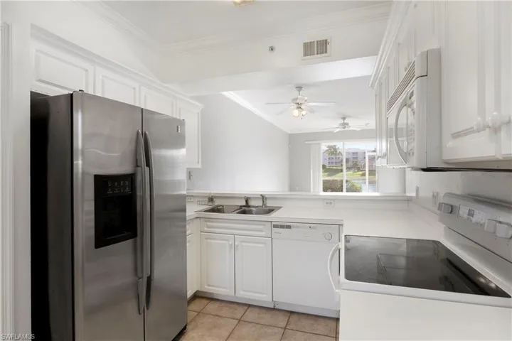 Kitchen with white appliances, crown molding, white cabinets, light tile patterned flooring, and light countertops