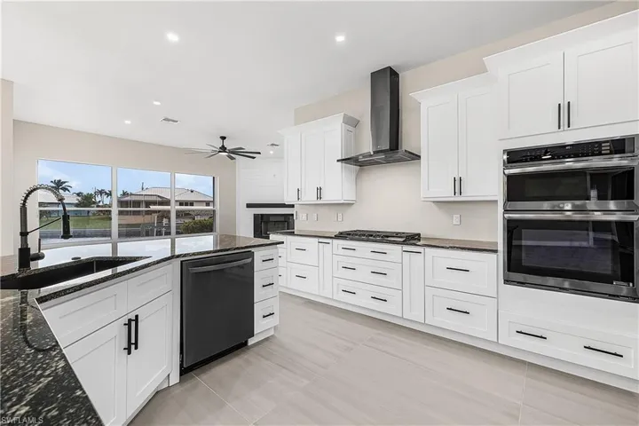 Kitchen featuring dark granite counters, stainless steel double oven, white cabinetry, and recessed lighting