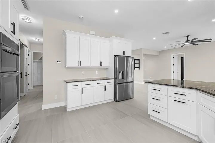 Kitchen with white cabinetry, appliances with stainless steel finishes, dark granite counters, and a ceiling fan
