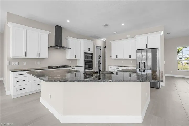Kitchen featuring dark granite counters, white cabinetry, wall chimney exhaust hood, a large island, and recessed lighting