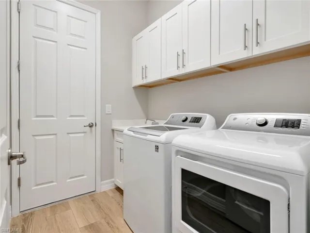 Laundry room featuring wood-finish tile  flooring, white shaker-style cabinetry, a solid-surface countertop, and a built-in sink