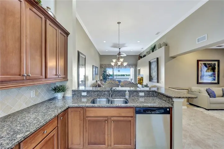 Kitchen with open floor plan, brown cabinets, stainless steel dishwasher, a peninsula, and a chandelier
