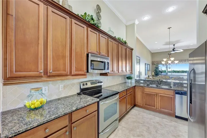 Kitchen featuring dark stone counters, appliances with stainless steel finishes, brown cabinets, backsplash, and crown molding