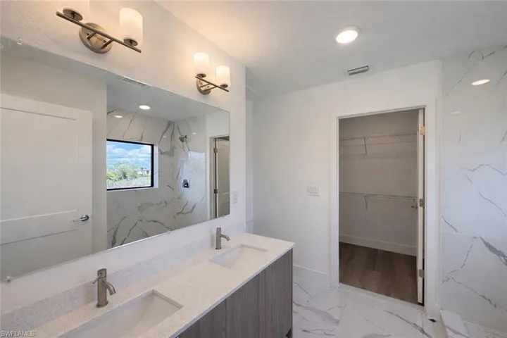 Full bath with light marble finish floors, a marble finish shower, double vanity, and a walk in closet