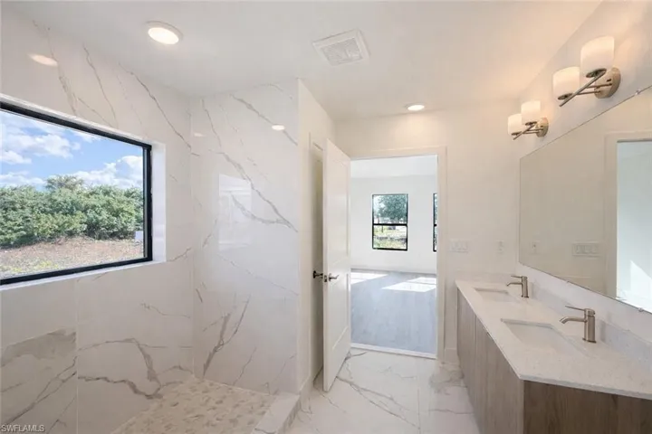 Full bathroom featuring light marble finish floors, double vanity, a marble finish shower, and recessed lighting