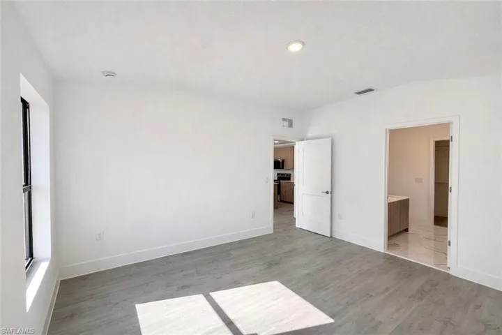 Unfurnished bedroom featuring light wood-type flooring, connected bathroom, and lofted ceiling