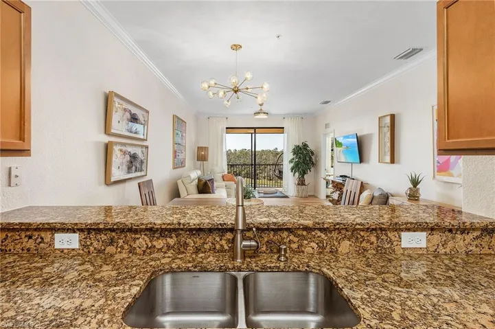 Kitchen with open floor plan, brown cabinets, dark stone countertops, a chandelier, and crown molding