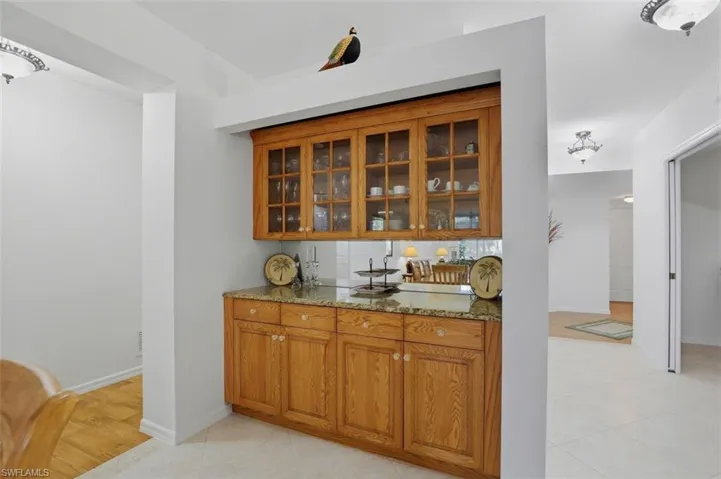 Bar area with light stone countertops, wood finish cabinets, glass insert cabinets, and light tile patterned floors