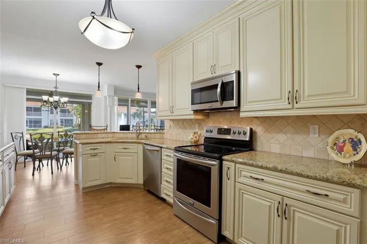 Kitchen with cream cabinets, stainless steel appliances, a peninsula, and light stone countertops