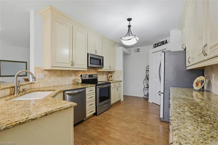 Kitchen with stainless steel appliances, light stone counters, hanging light fixtures, and light wood-style floors