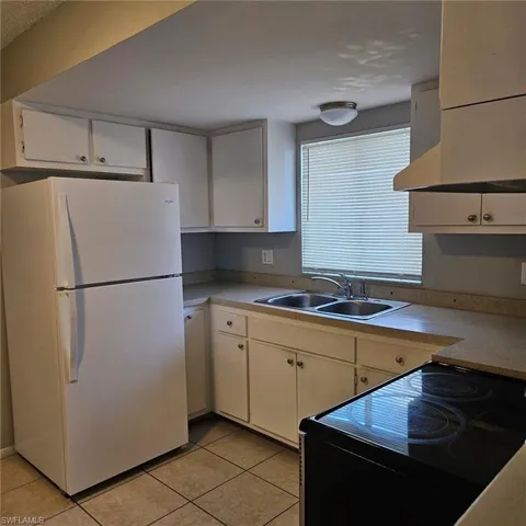 Kitchen featuring electric range, freestanding refrigerator, extractor fan, and white cabinets