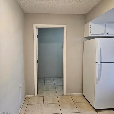 Kitchen with freestanding refrigerator, a textured ceiling, light tile patterned floors, and white cabinetry