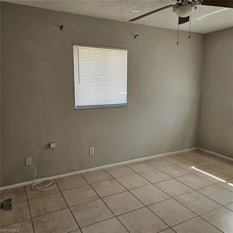 Empty room with ceiling fan, a textured ceiling, and light tile patterned floors