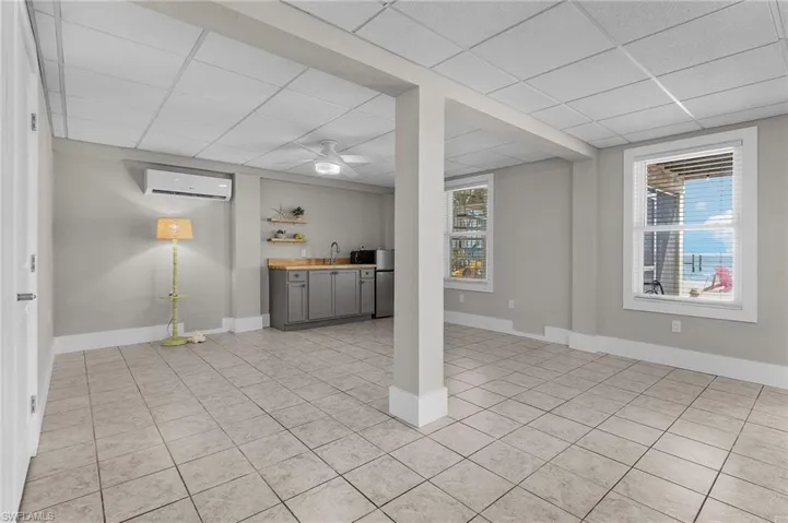 Basement featuring stainless steel fridge, an AC wall unit, bar, and a drop ceiling