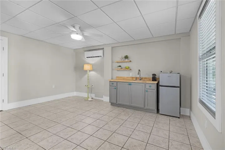 Bar with wood counters, an AC wall unit, stainless steel fridge, gray cabinets, and a drop ceiling