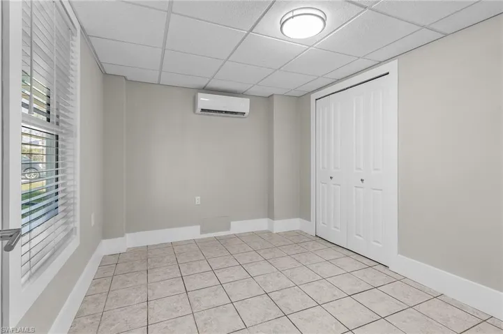 Basement with light tile patterned flooring, a paneled ceiling, and a wall unit AC
