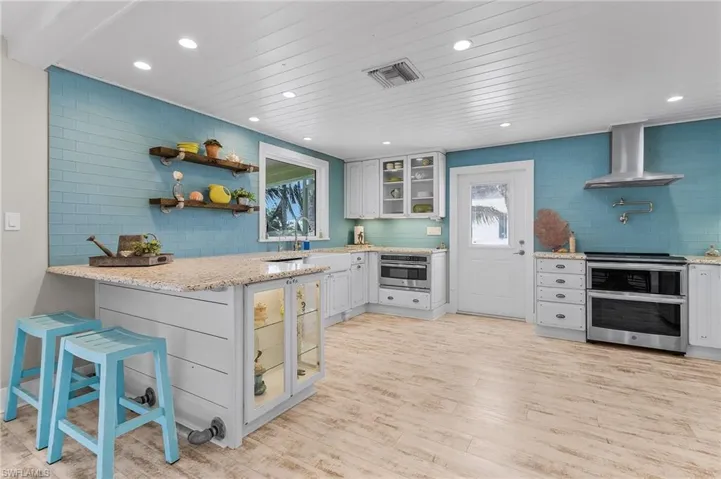 Kitchen with appliances with stainless steel finishes, white cabinetry, a kitchen breakfast bar, wall chimney range hood, and light wood-type flooring