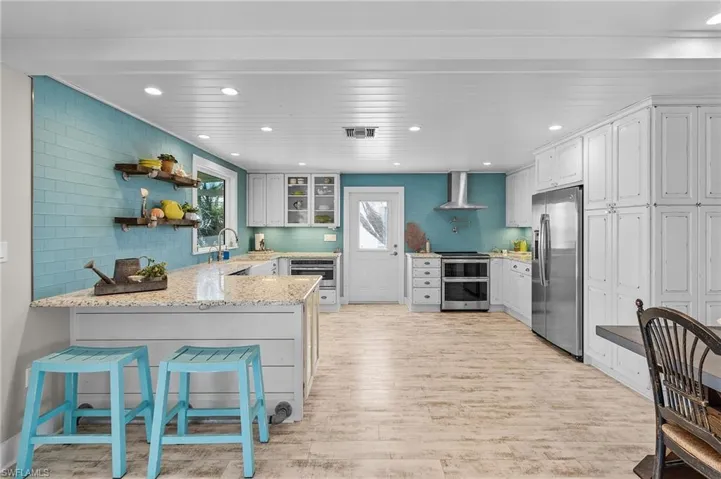 Kitchen with appliances with stainless steel finishes, white cabinets, a kitchen breakfast bar, kitchen peninsula, and wall chimney range hood