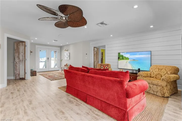 Living room featuring french doors, ceiling fan, wooden walls, and light hardwood / wood-style floors