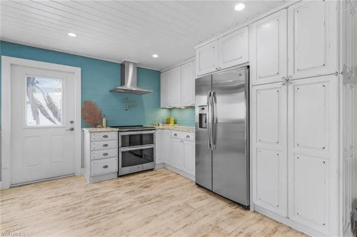 Kitchen featuring white cabinetry, stainless steel appliances, light hardwood / wood-style floors, and wall chimney range hood