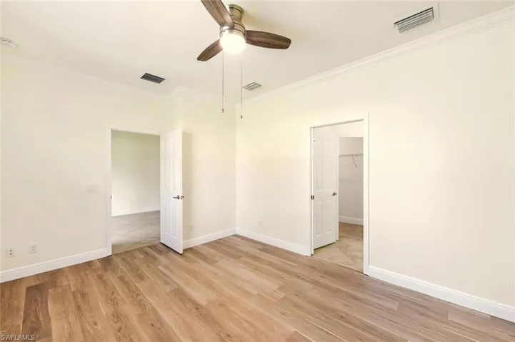 Unfurnished bedroom featuring ornamental molding, light wood-type flooring, a walk in closet, and a ceiling fan
