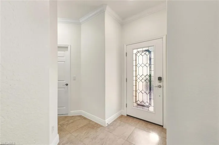 Foyer entrance with crown molding, a textured wall, and light tile patterned flooring