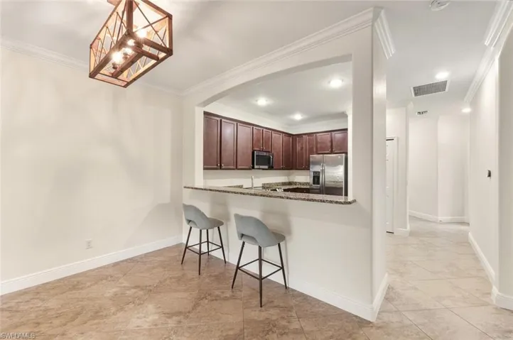 Kitchen with stainless steel appliances, dark stone counters, a kitchen bar, pendant lighting, and crown molding