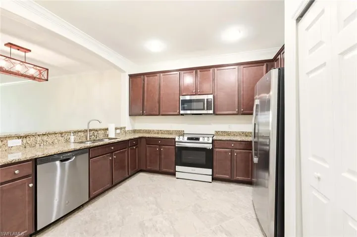 Kitchen with appliances with stainless steel finishes, light stone countertops, ornamental molding, pendant lighting, and dark brown cabinets