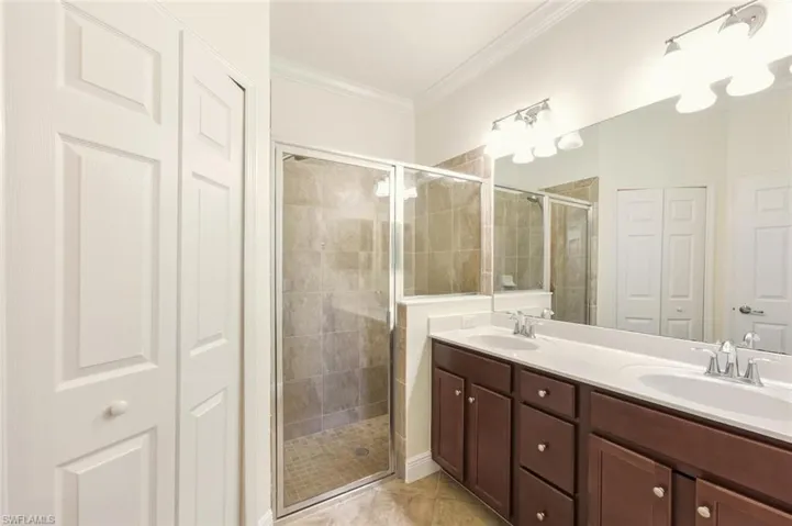 Full bath featuring a closet, double vanity, a shower stall, and crown molding