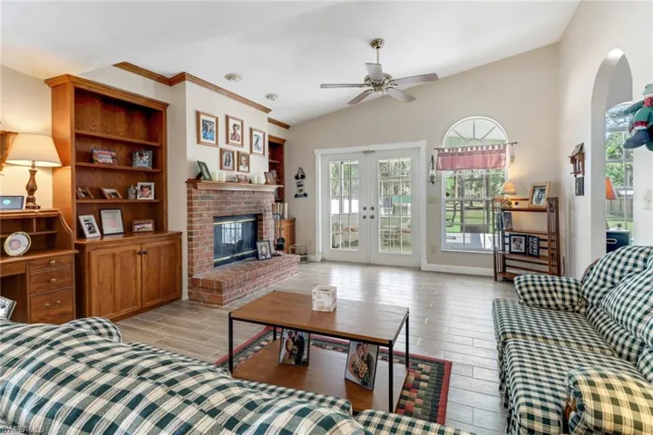 Living area with french doors, a fireplace, a ceiling fan, wood tiled floor, and vaulted ceiling