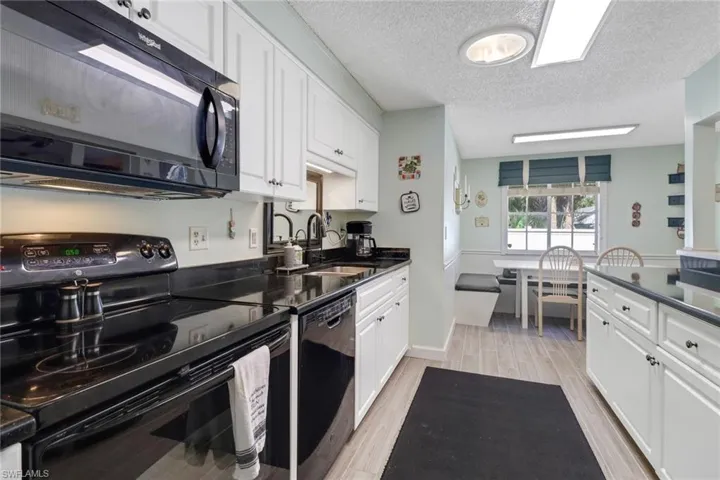 Kitchen with a sink, white cabinets, wood tiled floor, black appliances, and dark countertops