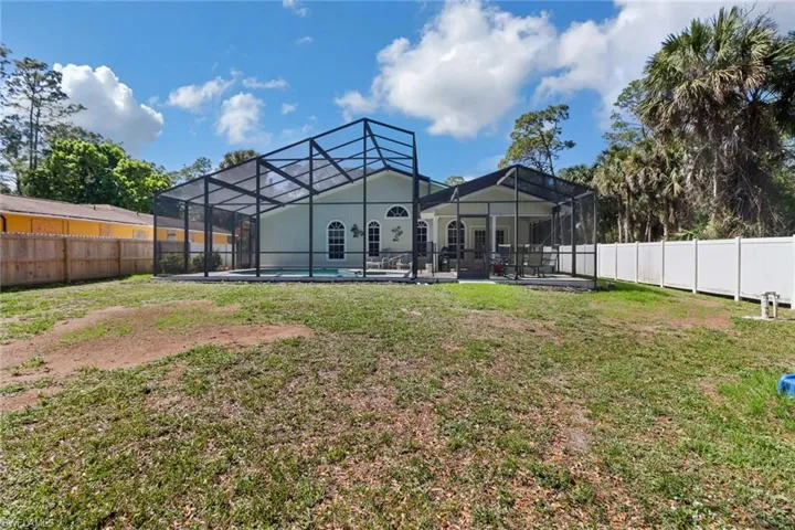 Back of house with a fenced in pool, glass enclosure, a fenced backyard, and a lawn