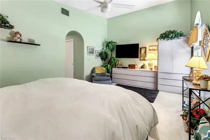 Carpeted bedroom with ceiling fan, visible vents, and arched walkways