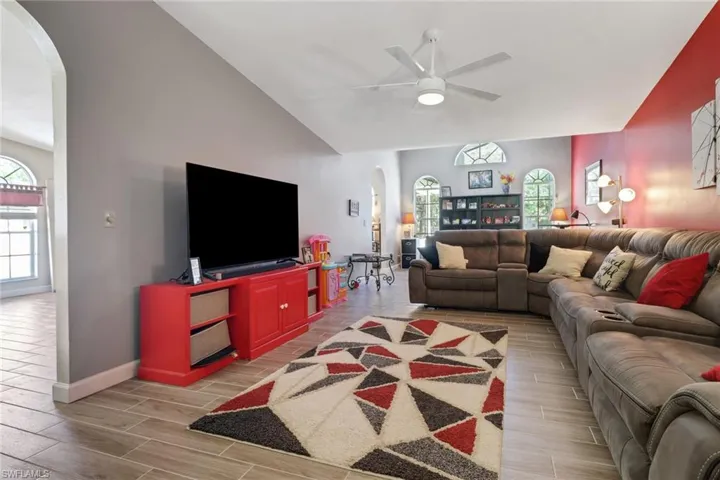 Living room with baseboards, arched walkways, a ceiling fan, wood finish floors, and high vaulted ceiling