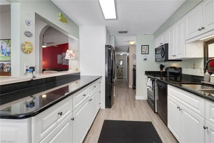 Kitchen featuring a sink, visible vents, white cabinets, wood tiled floor, and black appliances