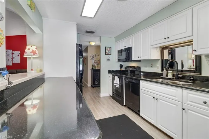 Kitchen featuring visible vents, white cabinets, light wood-style flooring, black appliances, and a sink