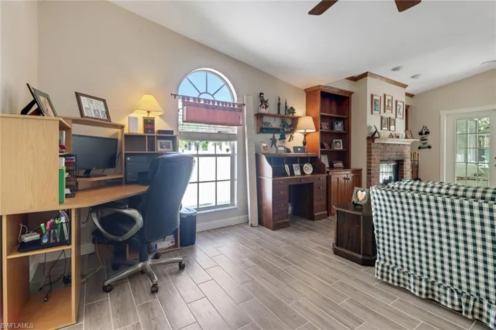 Office space with a brick fireplace, wood tiled floor, vaulted ceiling, and a wealth of natural light