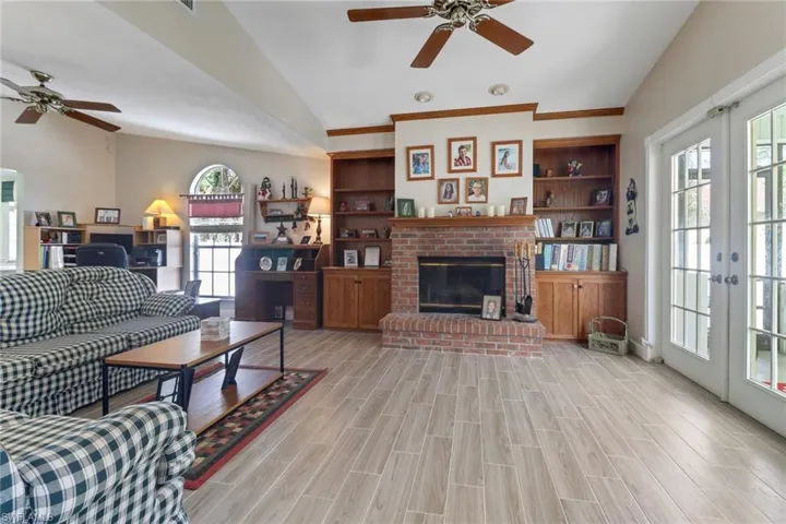 Living room with lofted ceiling, wood finish floors, french doors, a brick fireplace, and plenty of natural light
