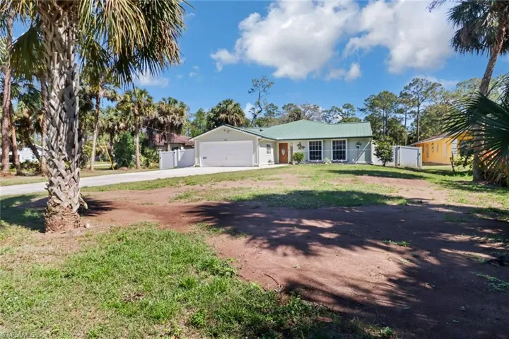 Single story home featuring concrete driveway, metal roof, an attached garage, fence, and a front lawn