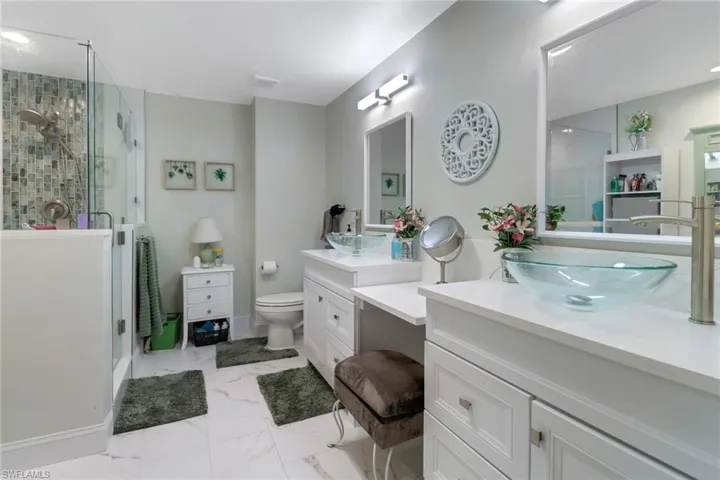 Full bathroom with toilet, two vanities, a sink, marble finish floor, and a shower stall