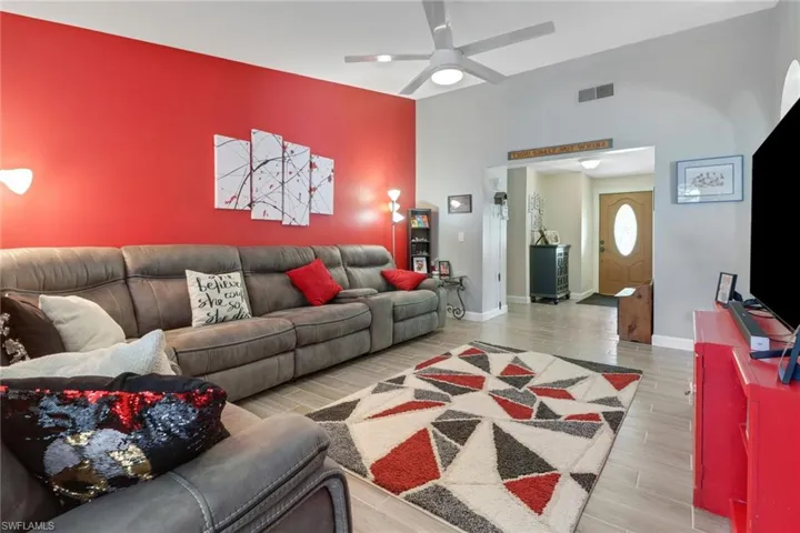 Living room with ceiling fan, an accent wall, wood finished floors, visible vents, and baseboards