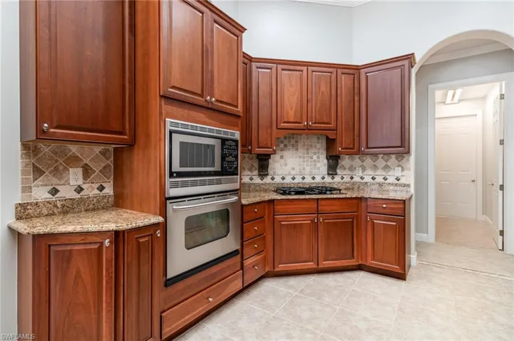 Kitchen with light stone countertops, stainless steel appliances, light tile patterned flooring, tasteful backsplash, and brown cabinets