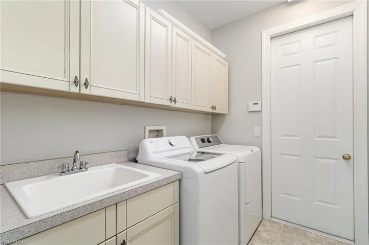 Laundry area with independent washer and dryer, light tile patterned flooring, and cabinet space
